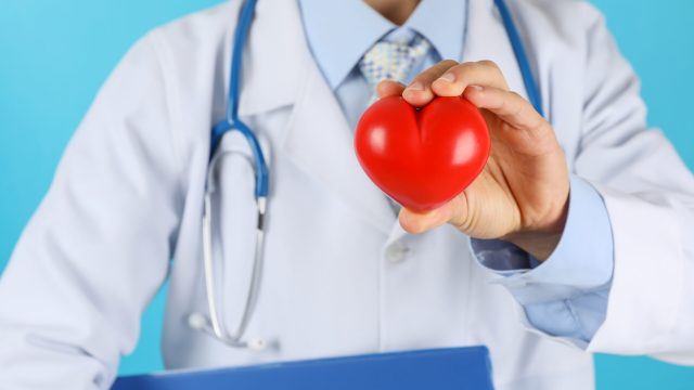 Doctor with stethoscope and heart against blue background, close