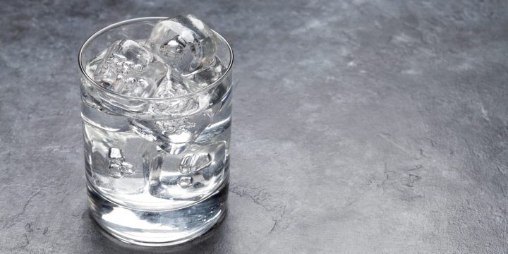 Glass of water with ice cubes on stone table. With copy space