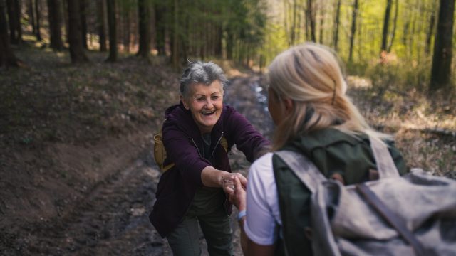 Senior women hikers outdoors walking in forest in nature, helping each other.
